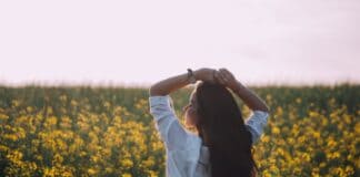 Woman in white shirt enjoying a sunny day in a blooming flower field.
