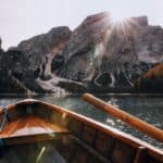 Wooden boat sailing on a serene mountain lake with sunrays illuminating the scenic landscape.