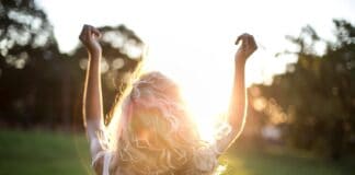 A woman with outstretched arms celebrates the sunset in a grassy field, capturing the essence of freedom and joy.
